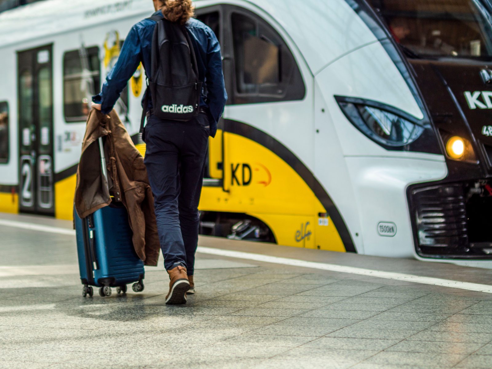 A traveller with a suitcase and backpack on a train platform, mid-journey.