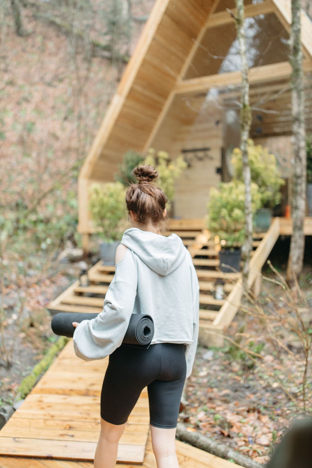 A traveller walking toward a wellness retreat cabin, yoga mat in hand, representing the wider wellness universe, digitally connected.
