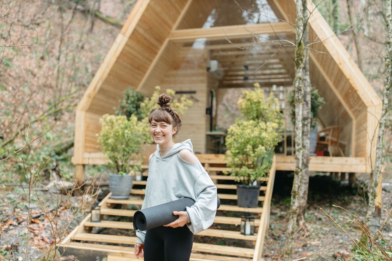 A traveller smiling, yoga mat in hand, arriving at a wellness retreat cabin.